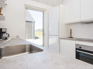 Een moderne keuken met een roestvrijstalen spoelbak, witte kasten, een inbouwoven en uitzicht door een schuifdeur.