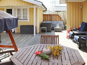En träaltan med ett bord, stolar och en överbyggd grillplats.