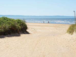 A sandy beach path leading to the ocean with a clear view of the sea and distant hills.