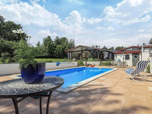 A swimming pool with a covered patio area, a table with a potted plant, and a chair. - 5 Person Holiday Home in Frederiksvaerk (Frederiksvaerk)