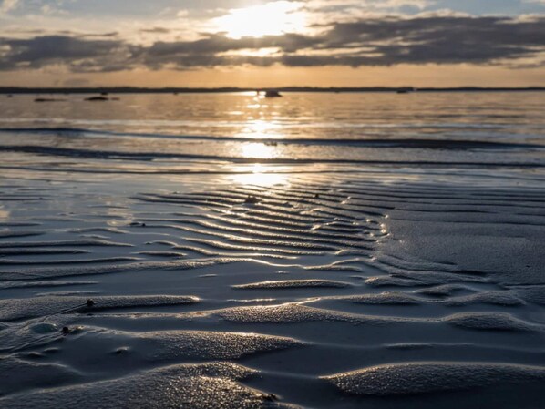 A beach with gentle waves and a sunset in the background.