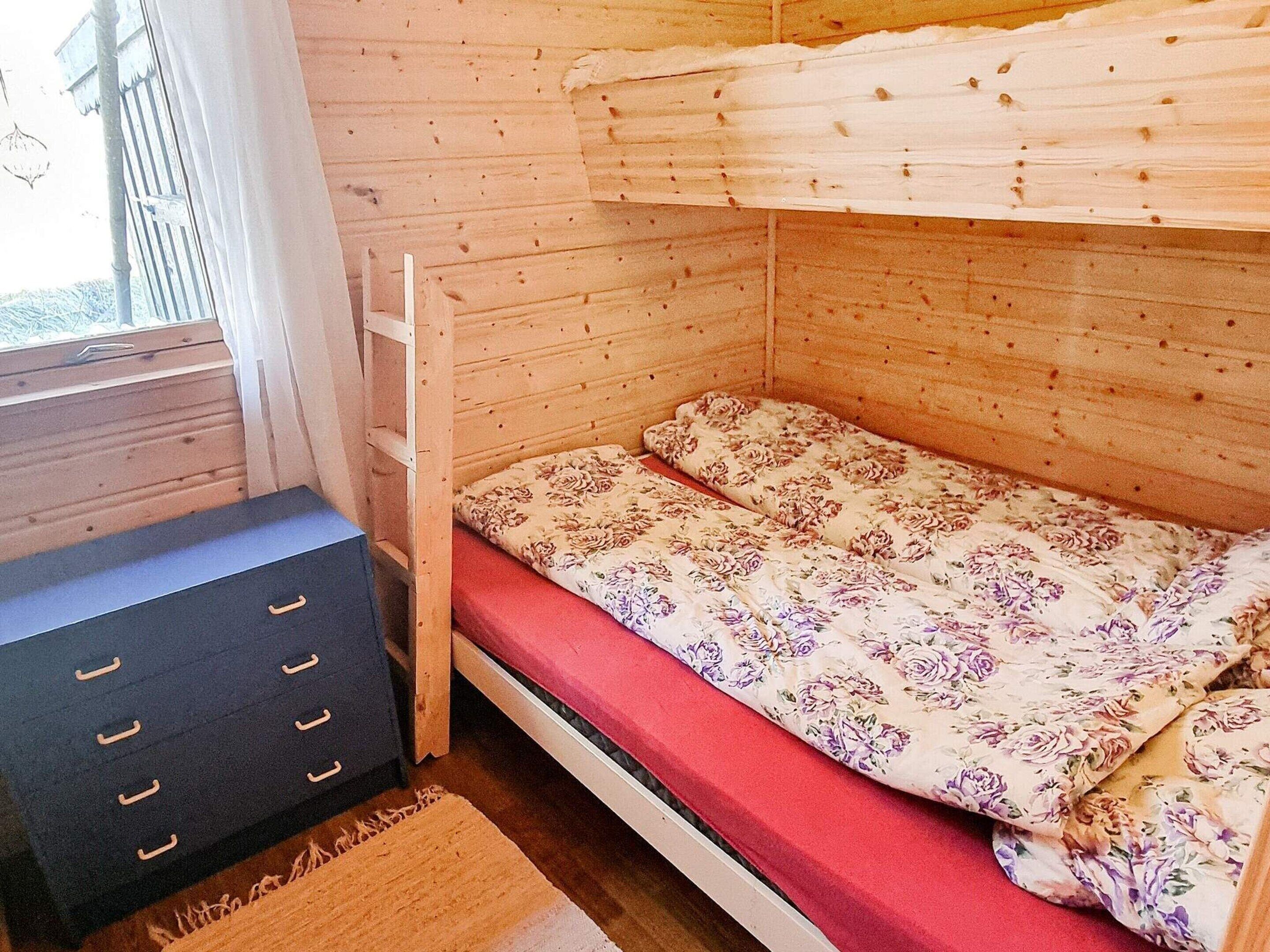 A small, single-bed room with a wooden bunk bed, a black dresser with drawers, and a window with curtains.