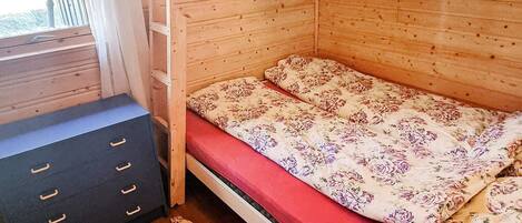 A small, single-bed room with a wooden bunk bed, a black dresser with drawers, and a window with curtains.