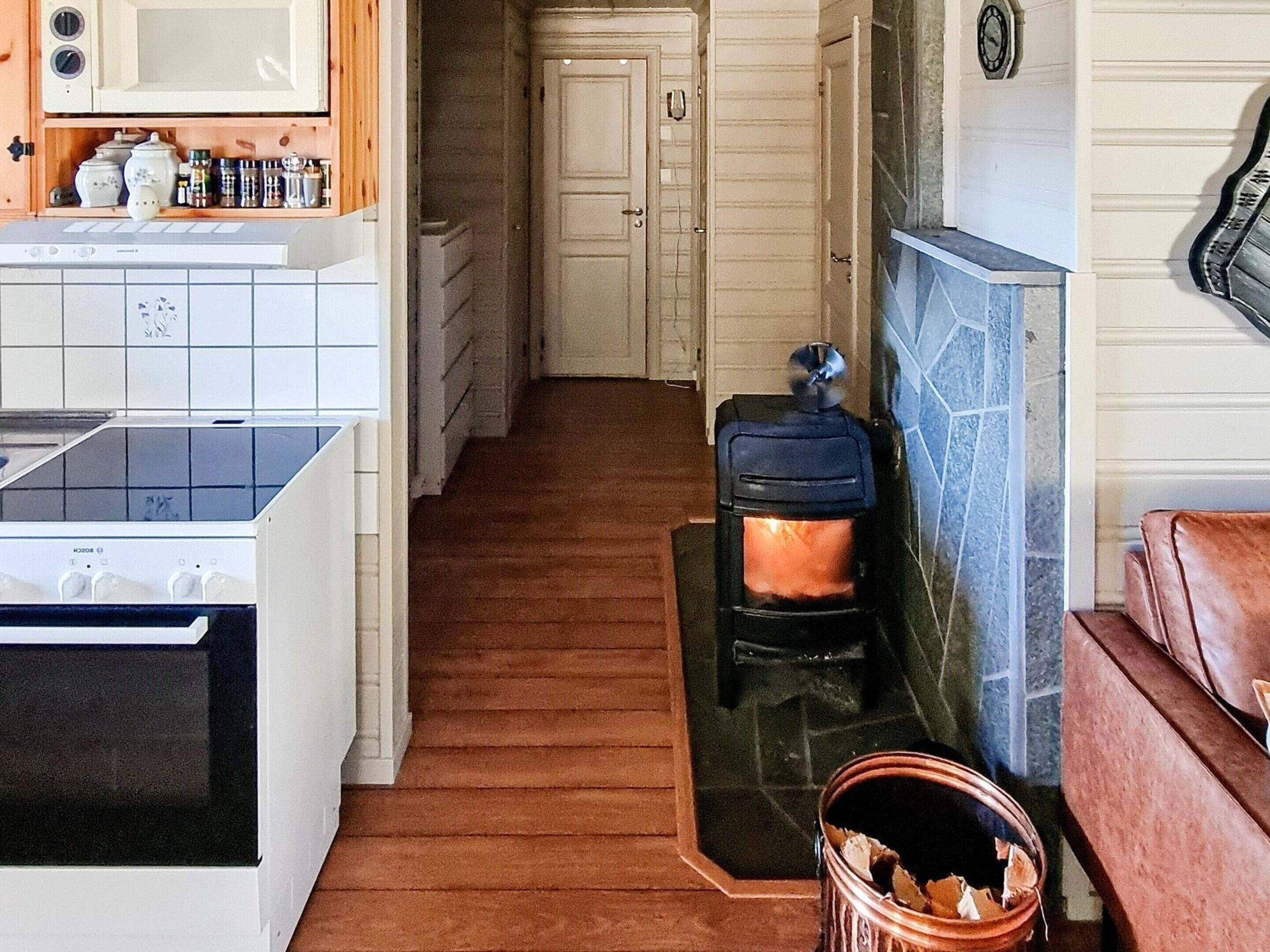 A narrow hallway with a kitchen area on one side, a fireplace on the other, and a wooden bench in the foreground.