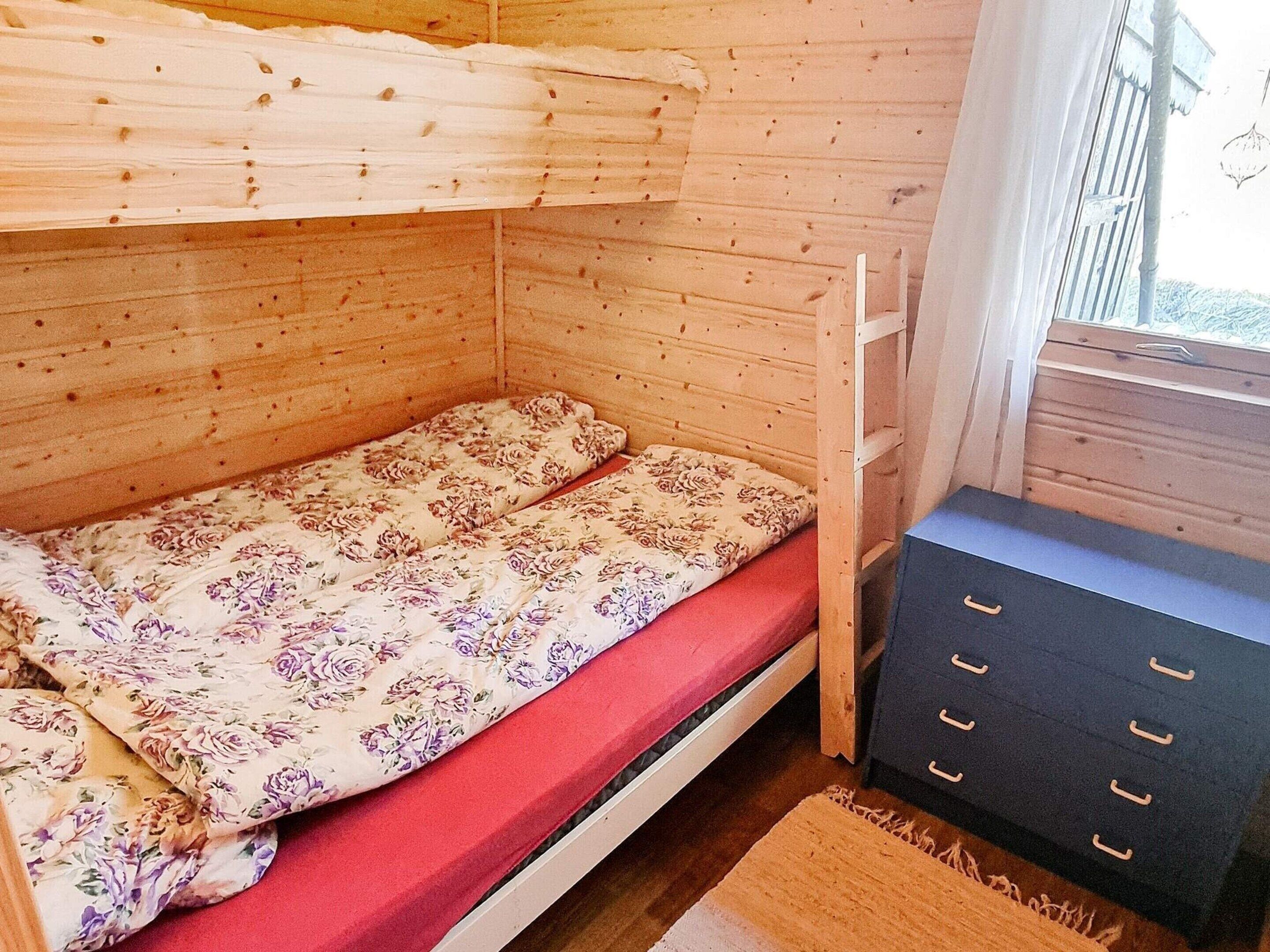 A bunk bed with floral bedding, a wooden dresser, and a window with a view.
