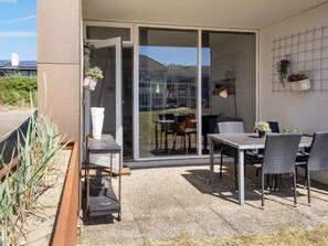 An outdoor patio with a table and chairs, a sliding glass door leading to a backyard, and a wall-mounted plant holder. - 2 Person Holiday Home in Ringkobing (Ringkobing)