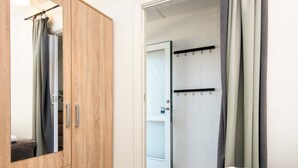 Een kamer met een houten garderobe, een deur naar een badkamer, en een bed met een wit kussen.