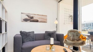 Een moderne woonkamer met een grijze bank, een ronde houten salontafel, een afstandsbediening en een decoratieve fauteuil met een bont plaid.