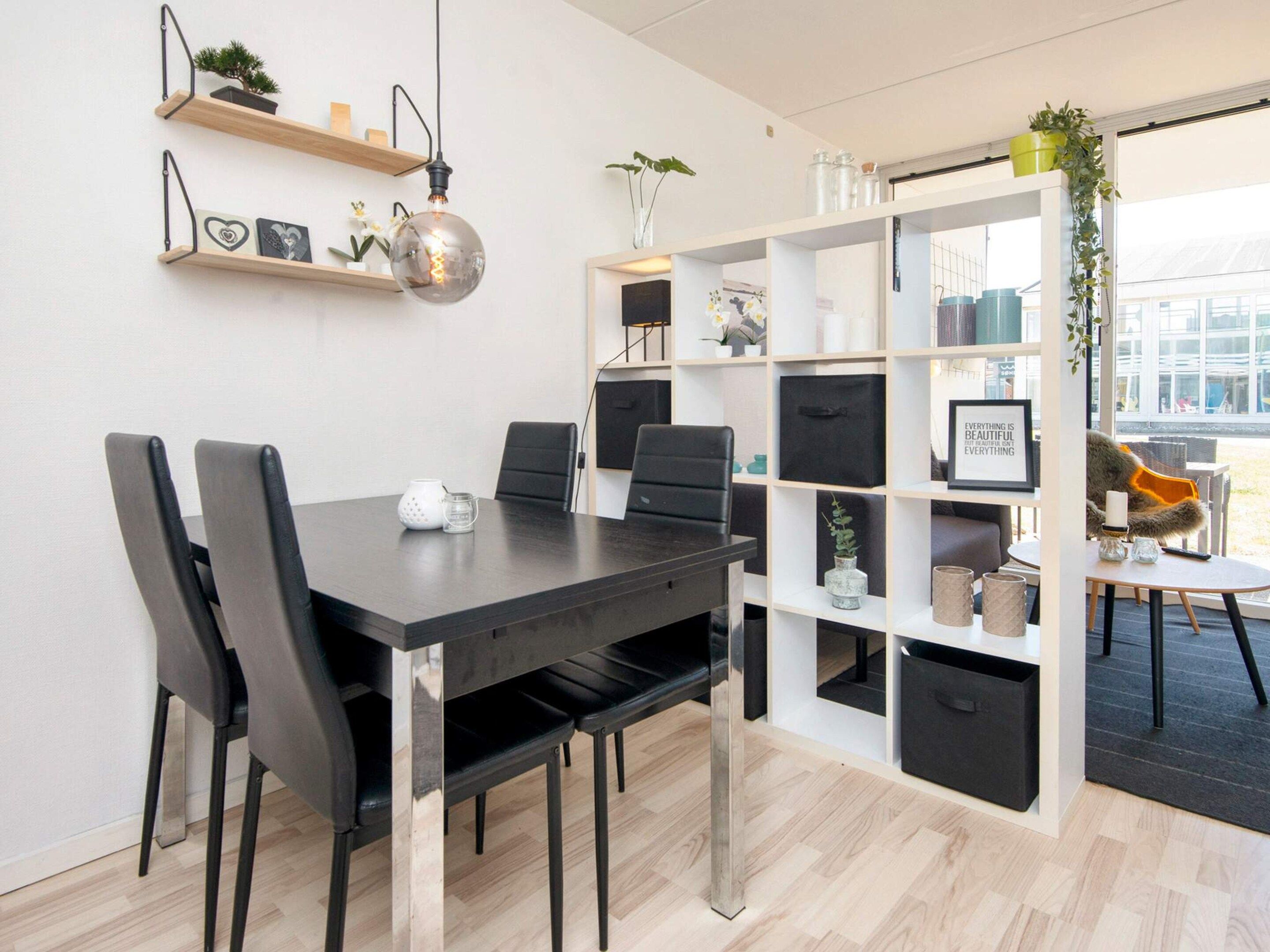 Un espacio de oficina moderno con una mesa de madera oscura, sillas negras y una estantería blanca con diversos objetos.