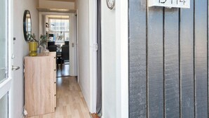 Een gang met een houten vloer, een spiegel, een klok en een deur met de aanduiding 'D114'.