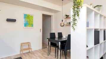 Ein modernes Wohnzimmer mit Essbereich, einer Karte an der Wand, einem kleinen Holzschemel und einer weißen Regaleinrichtung mit Pflanzen.