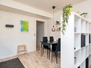 Un espacio de estar moderno con comedor, un mapa en la pared, un taburete de madera y una estantería blanca con plantas.