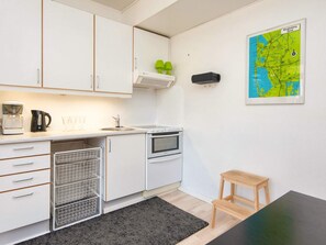 A compact kitchen with white cabinets, a stove, a sink, and a coffee maker. - 2 Person Holiday Home in Ringkobing (Ringkobing)