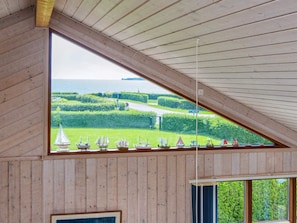A room with a sloped ceiling and a large window overlooking a green landscape and the sea. - 4 Star Holiday Home in Juelsminde (Horsens)