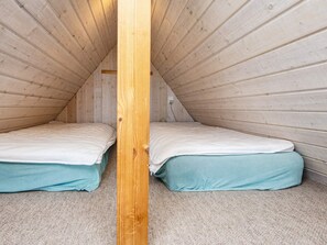 A small, enclosed room with two beds aligned against the sloped ceiling, wooden walls, and a carpeted floor.