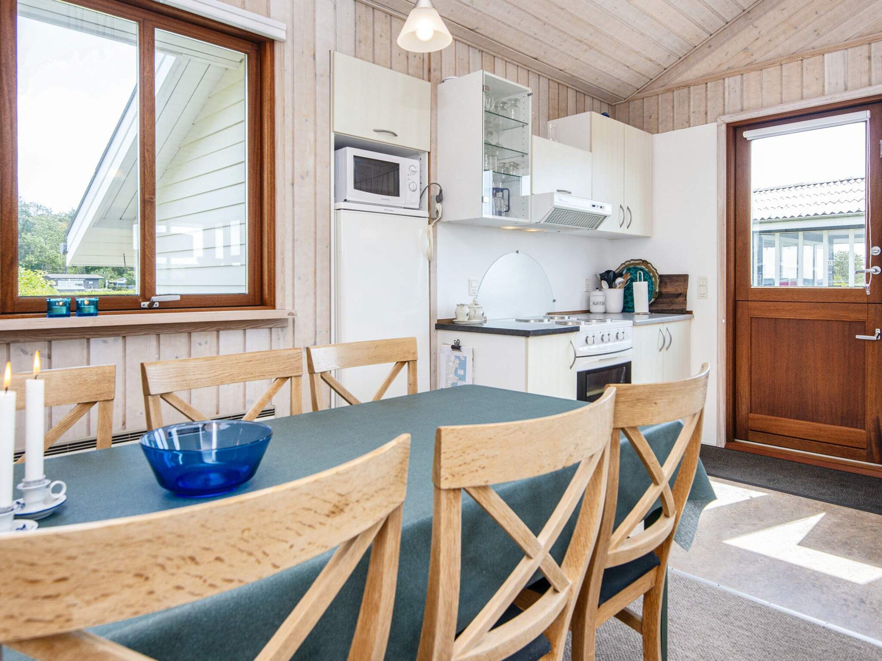 A compact kitchen with white cabinets, a microwave, and a stove. There is a dining table with chairs and a blue bowl on it.