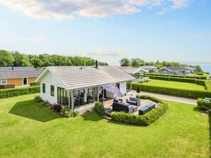 A single-story house with a covered patio, a lawn, and a view of the sea. - 4 Star Holiday Home in Juelsminde (Horsens)