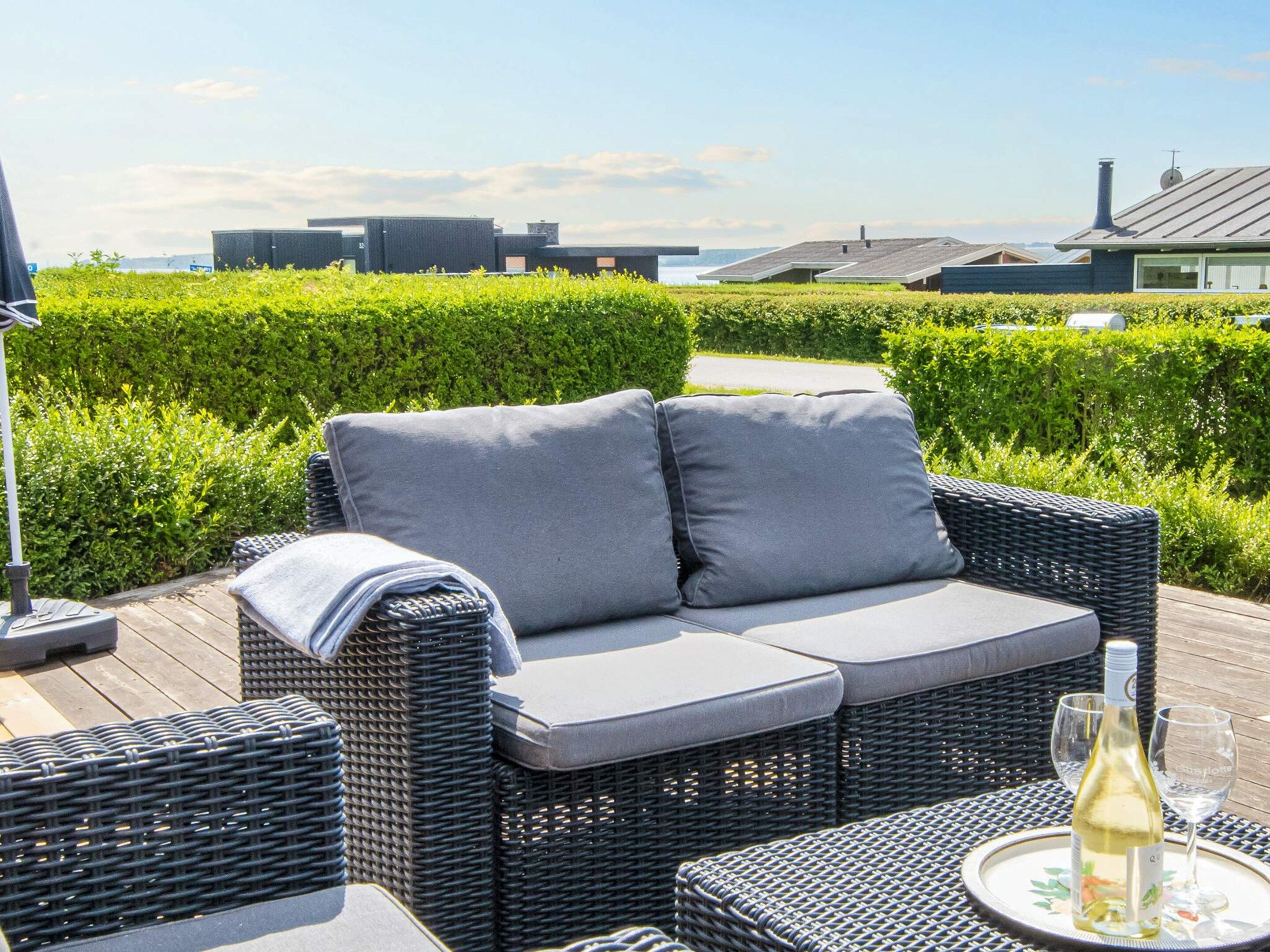 En fletsofa med puder, et bord med en flaske hvidvin og et glas, samt udsigt til bygninger og et vandområde.