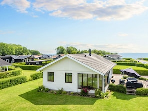 A single-story house with a large glass window, surrounded by well-maintained lawns and hedges, with a view of the sea in the background. - 4 Star Holiday Home in Juelsminde (Horsens)