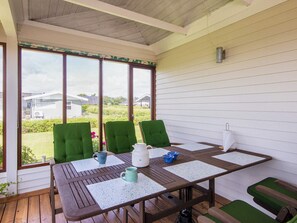 Une terrasse couverte avec une table, des chaises et une vue sur les environs.