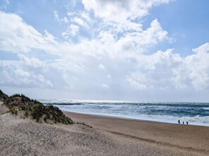 Une plage avec un rivage sablonneux et des vagues, sous un ciel partiellement nuageux.