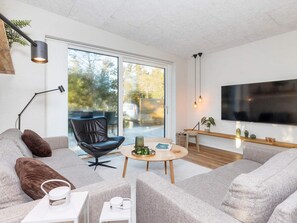 A modern living room with a sofa, a coffee table, a TV, and a large window. - 5 Star Holiday Home in Vestervig (Vestervig)