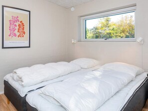 Une chambre à coucher avec un lit, une fenêtre donnant sur des arbres et une œuvre d’art encadrée accrochée au mur.