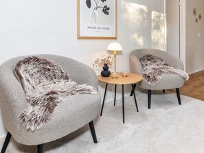 A room with two grey armchairs with fur throw pillows, a small round table with a lamp, and a framed artwork on the wall. - 5 Star Holiday Home in Vestervig (Vestervig)