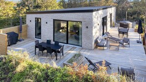 A modern outdoor deck with a dining area, lounge seating, and a hot tub. - 5 Star Holiday Home in Vestervig (Vestervig)
