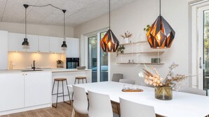A modern kitchen with white cabinetry, a central island, pendant lighting, and a dining area with a white table and chairs. - 5 Star Holiday Home in Vestervig (Vestervig)