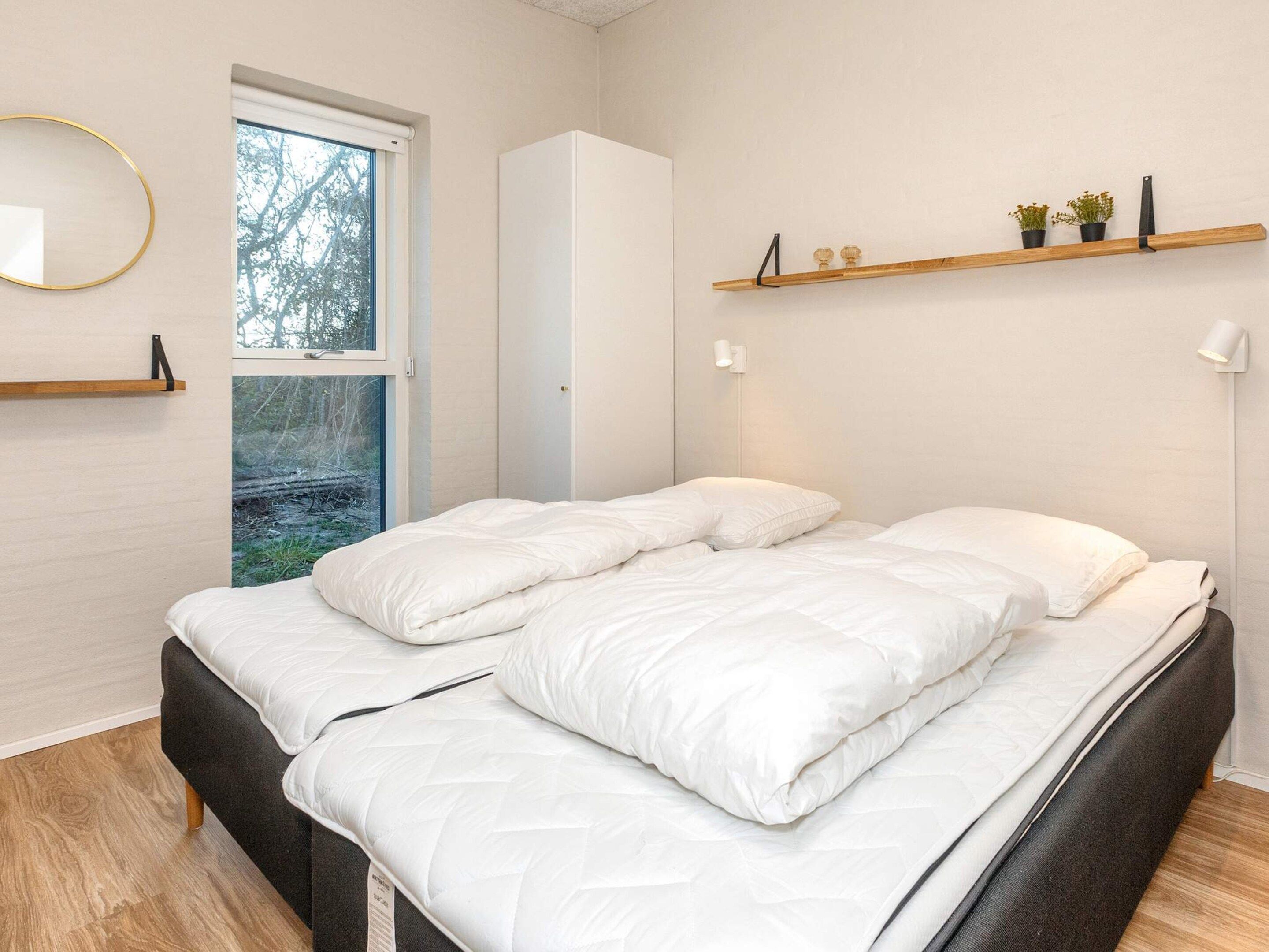 A bedroom with a bed, a window, a wall-mounted shelf with plants, and a bedside lamp.