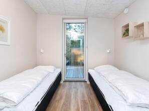 A bedroom with two beds, a sliding glass door to a balcony, and a small shelf with a plant. - 5 Star Holiday Home in Vestervig (Vestervig)