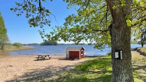 A lakeside picnic area with a red shed, a picnic table, and a trail leading to the water. - 4 Star Holiday Home in Sparreholm (Sparreholm)