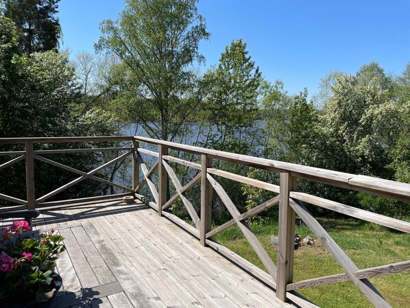 Une terrasse en bois, dotée de rampes de protection, qui offre une vue sur une étendue d’eau et est entourée d’arbres.