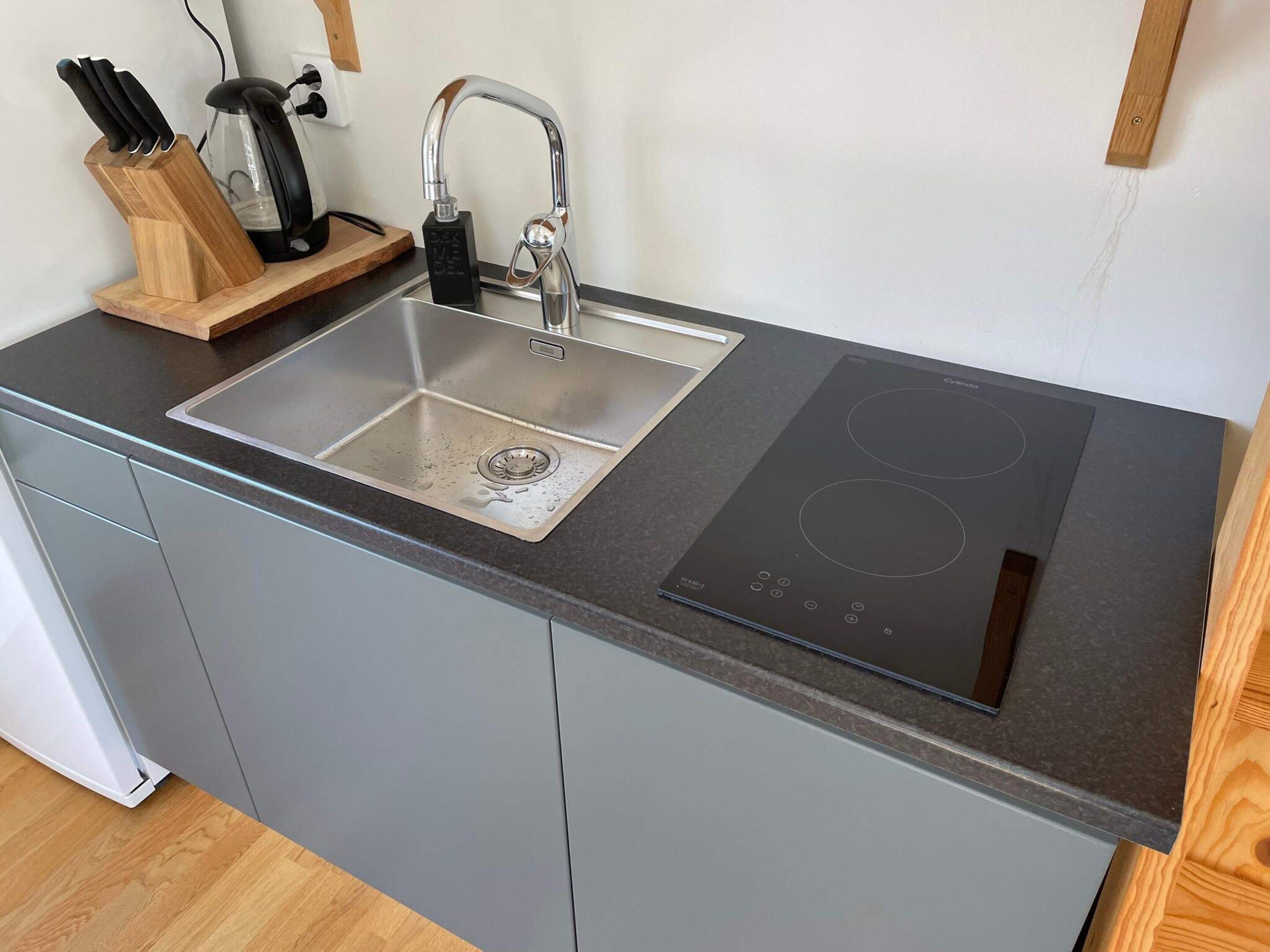 Una cocina con un lavamanos de acero inoxidable, una estufa eléctrica negra y un bloque de cuchillos de madera.
