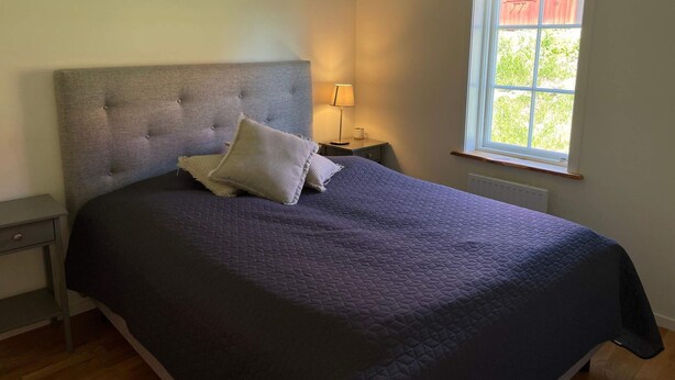 A bedroom with a large bed, a nightstand, a lamp, and a window with a view of greenery. - 4 Star Holiday Home in Sparreholm (Sparreholm)