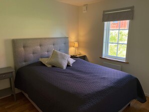 A bedroom with a large bed, a nightstand, a lamp, and a window with a view of greenery. - 4 Star Holiday Home in Sparreholm (Sparreholm)