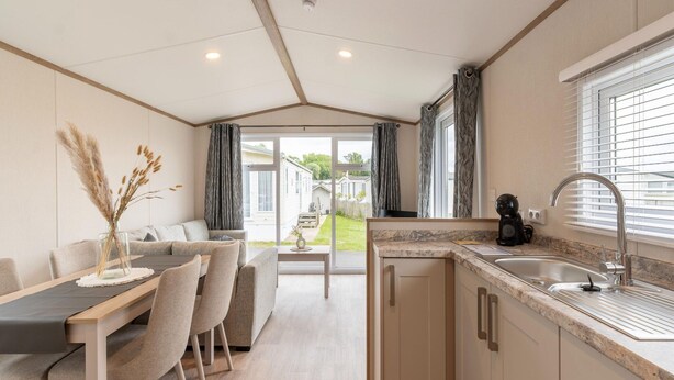 A modern kitchen with a sink, countertop, and cabinets. There is a dining area with a table and chairs. - Chalet in De Haan Near Sandy Beaches (De Haan)