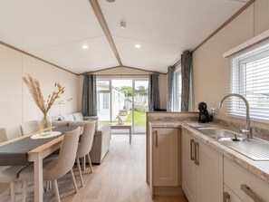 A modern kitchen with a sink, countertop, and cabinets. There is a dining area with a table and chairs. - Chalet in De Haan Near Sandy Beaches (De Haan)