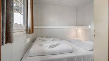 A small, single-bed room with white walls and a window with curtains.