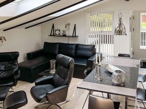 A modern living room with a black leather sofa, a glass-top dining table, and a chandelier.