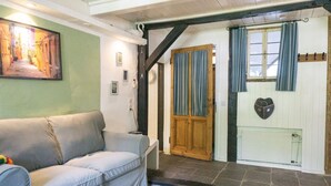 Un salon chaleureux avec un canapé, un tableau, une porte en bois et un sol en pierre.