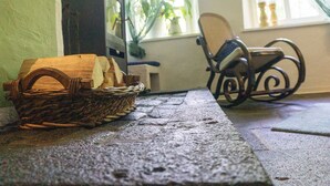 Une pièce avec une table en bois, un panier en osier contenant du pain, un téléviseur, une chaise et une fenêtre ornée de plantes.