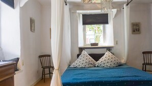 Une chambre à coucher avec un lit, une fenêtre, une chaise et une commode en bois.
