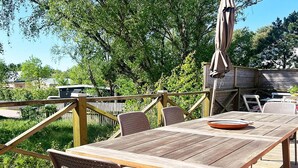 A wooden deck with a table and chairs, surrounded by greenery and trees. - Attractive Apartment With Terrace-by Traum (Mellbystrand)