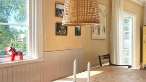 A dining area with a wooden table, two candles, a wicker lamp, and a window with a red horse decoration. - Attractive Apartment With Terrace-by Traum (Mellbystrand)