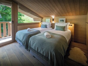 Une chambre avec deux lits, des murs en bois, un balcon et une fenêtre.