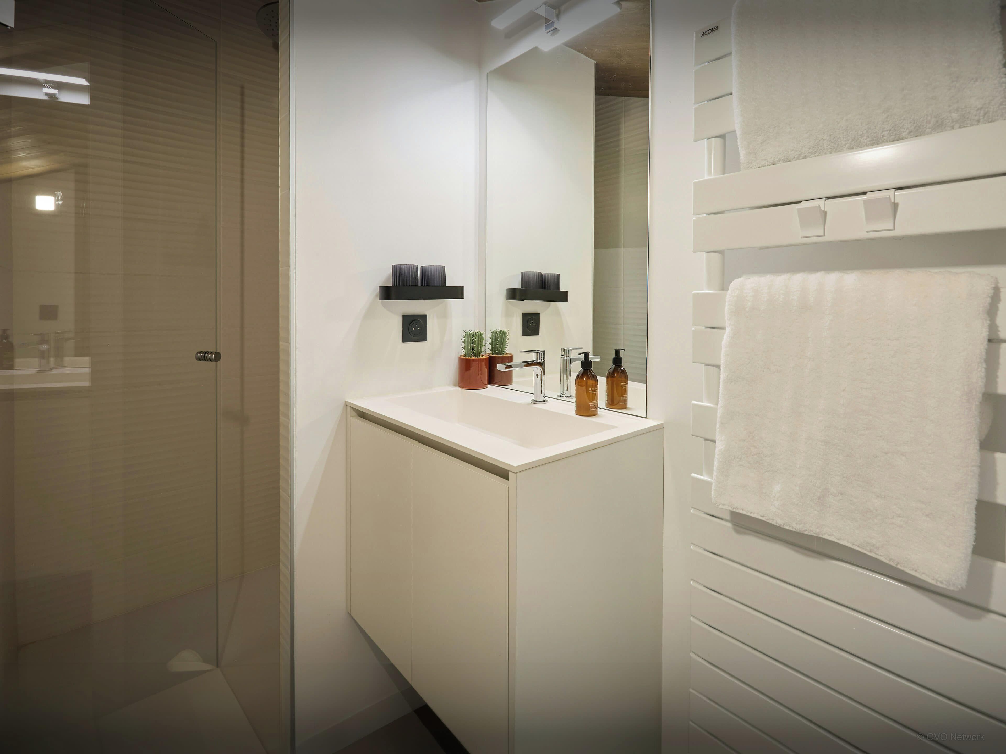 Een moderne badkamer met een douchecabine van glas, een witte wastafel met spiegel en een handdoekrek.