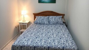 A bedroom with a wooden bed, a nightstand with a lamp, and a painting of a waterfall on the wall. - Beachhouse Gran Tarajal 3BR (Gran Tarajal)