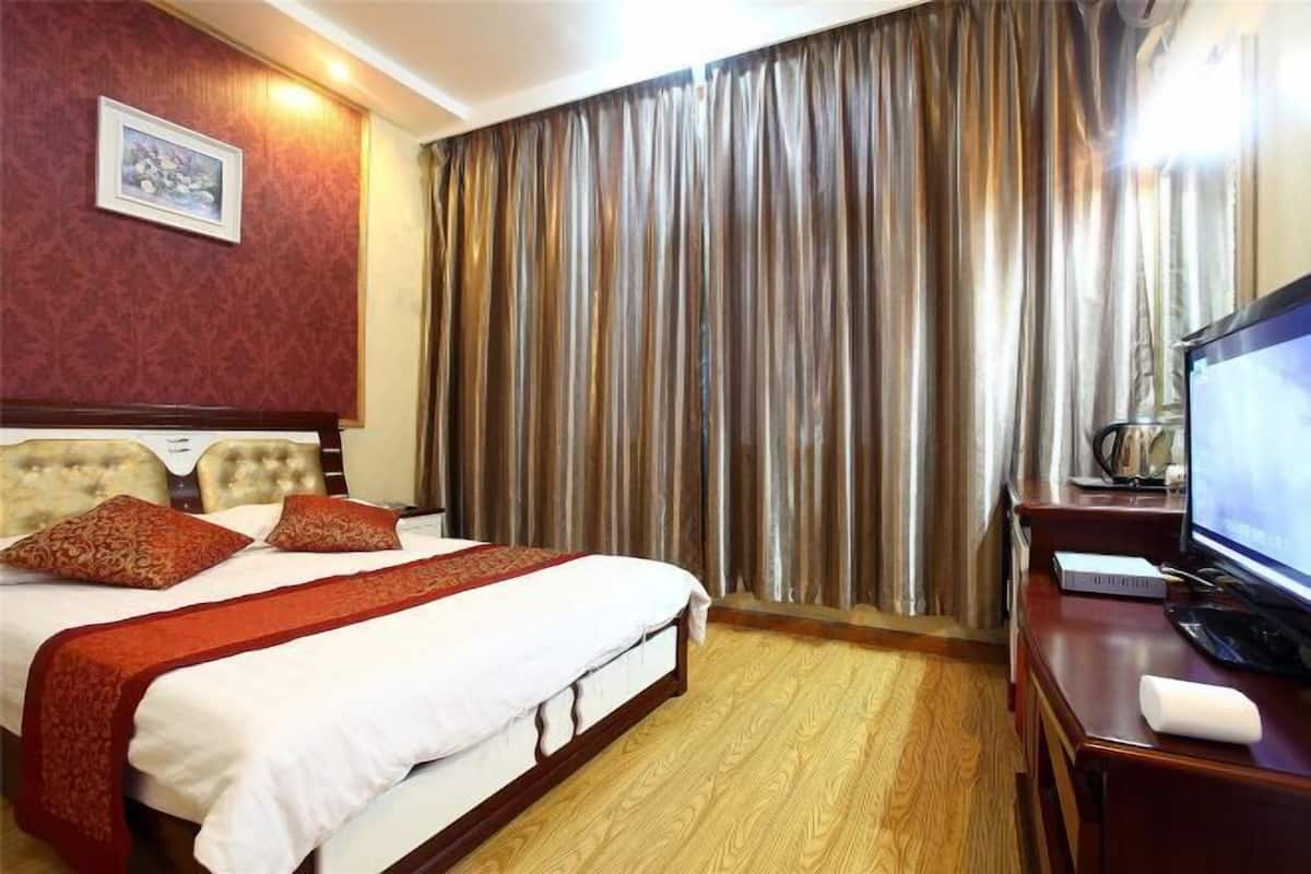 Une chambre d’hôtel avec un lit, un bureau équipé d’un ordinateur, une télévision et une grande fenêtre avec des rideaux.